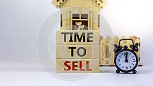 Time to sell real estate. Wooden blocks form the words `time to sell` near miniature house. Black alarm clock. Beautiful white