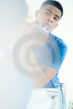 Time to shave this all off. Shot of young man shaving his face in his bathroom mirror.