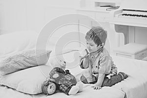 Time to sleep concept. Child in bedroom with silence gesture. Boy with happy face puts favourite toy on bed, time to