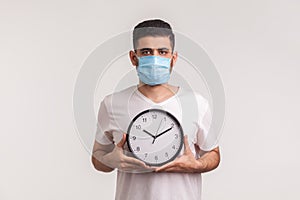 Time to stop coronavirus. Man in protective hygienic mask holding clock, warning of novel virus epidemic