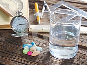 Time to take medicine. Pocket watch, Colorful medicine, water glasses, stationery and stationery. On the old wood table, meaning d