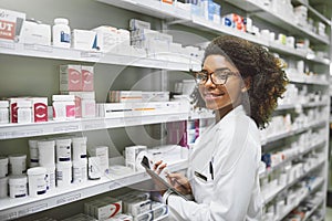 Time to take your meds. Portrait of a cheerful young female pharmacist holding a digital tablet while looking at the