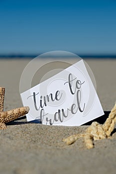 TIME TO TRAVEL text on paper greeting card on background of starfish seashell summer vacation decor. Sandy beach sun