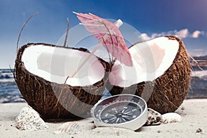Time to travel. Two halves of a coconut with an umbrella and a compass on the beach against the background of the sea and sky.