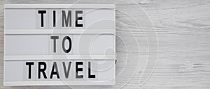 `Time to travel` words on a modern board on a white wooden background, top view. Overhead, from above, flat lay. Copy space