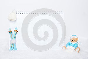 Time for winter holidays. Blank notepad, teddy bear with snowballs, toy wooden blue skis and white hat on snowy