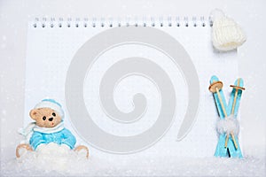 Time for winter holidays. Blank notepad, teddy bear with snowballs, toy wooden blue skis and white hat on snowy