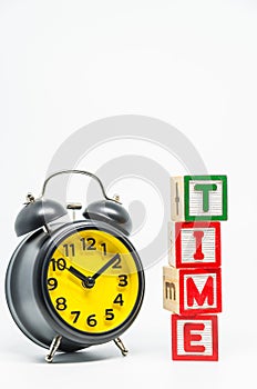 TIME word wooden block arrange in vertical style with black retro alarm clock on white background and selective focus