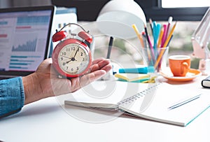 Time and work concepts with male hand holding alarm clock on desk