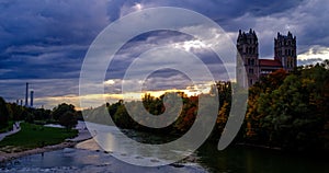 Timelapse of Munich at dramatic sunset - Isar river, trees, church. Munchen, Bavaria, Germany. Camera zoom in