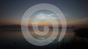 Timelapse silvery mesospheric clouds above the lake float and are reflected in the water