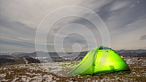 Timelapse, tent on a winter night on a mountain top with a view of the village in the carpathian mountains