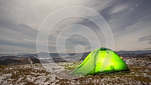 Timelapse, tent on a winter night on a mountain top with a view of the village in the carpathian mountains