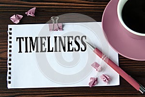 TIMELINESS - word on a white sheet on a wooden brown background with a cup of coffee and a pen