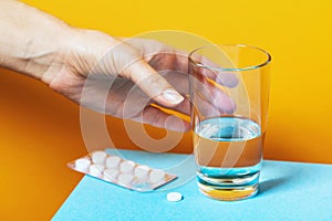 Timely medication is a guarantee of the health of the body. A hand reaches for a glass of water to drink a pill