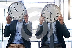 Times a wasting. two businessmen holding clocks over their faces in the office.