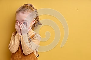 Timid little girl being shy, covering eyes. Cute female child kid playing seek and hide