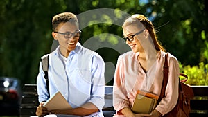 Timid students in glasses trying to make acquaintance, sitting on bench in park