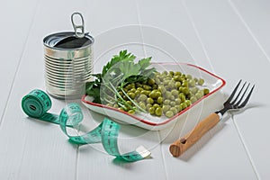 Tin can, green peas, fork and measuring tape on a wooden table.