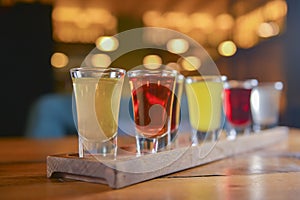 Tincture alcoholic in small shot glasses. Natural fruit alcohol drinks, shots served on a wooden table