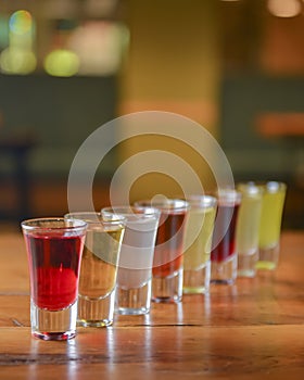 Tincture alcoholic in small shot glasses. Natural fruit alcohol drinks, shots served on a wooden table