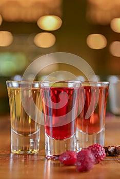 Tincture alcoholic in small shot glasses. Natural fruit alcohol drinks, shots served on a wooden table