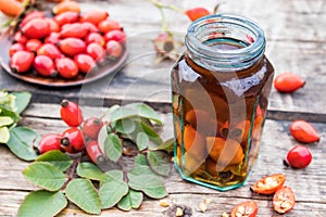 Tincture or drink with wild rose in a glass bottle near ripe red rosehip berries photo