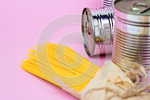 Tinned food, metal cans and yellow spaghetti pasta on pink background with copy space. Grocery donation, charity and delivery