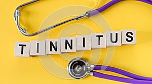 Tinnitus written from wooden blocks with Stethoscope on yellow background