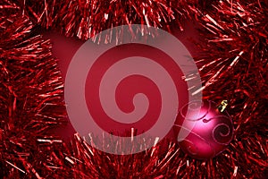 Tinsel with ball on red background. Space for text