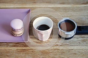 Tiny coffee pink ceramic cup, macarons, coffee holder on wooden table or background.