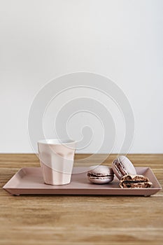 Tiny coffee pink ceramic cup and macarons on wooden table or background, white wall behind