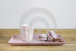 Tiny coffee pink ceramic cup and macarons on wooden table or background, white wall behind