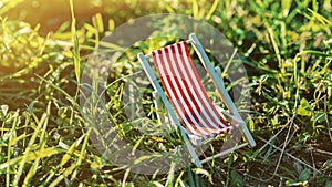 Tiny colorful toy deckchair in grass. Summer vacation concept. Sunset time. Children dreaming of holiday rest. Small toy on lawn.