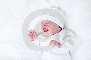 Tiny crying newborn baby in knitted hat and jacket