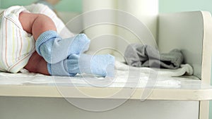 Tiny Cute Newborn Babies Feet In Blue Socks Early First Days Of Life On White Background. Close up of Small Legs of Baby