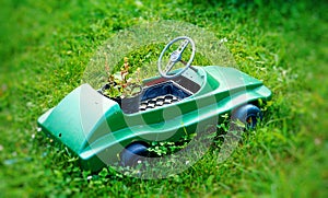 Tiny decorative plastic vehicle with flower pot on green lawn.