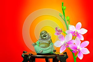 Tiny figurine of laughing buddha and pink orchid flowers
