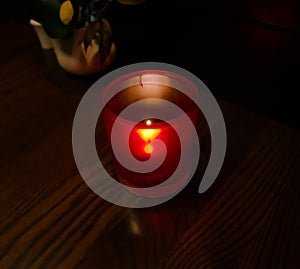 A tiny flame flickers in a red translucent votive candle holder, illuminating a glossy wooden table top