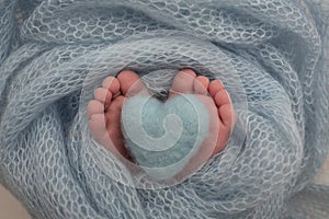 The tiny foot of a newborn baby. Soft feet of a new born in a blue blanket. Knitted blue heart in the legs of a baby.