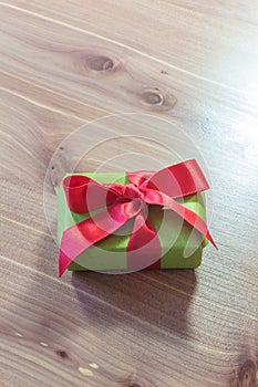Tiny gift box wrapped in green paper with a big red satin bow, copy space, neutral wood background