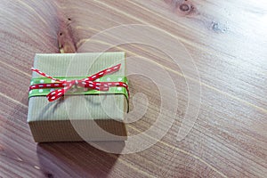 Tiny gift box wrapped in rustic brown kraft paper with red and green ribbons, simple bow