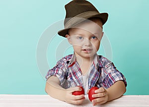 Tiny little boy in a hat looks on viewer in hands holding red Ea