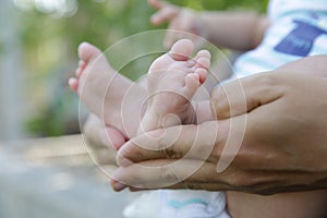 Tiny newborn baby foot in his mother`s palm in warm colors in soft focus background. Hands of mother and baby foot.