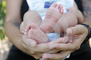 Tiny newborn baby foot in his mother`s palm in warm colors in soft focus background. Hands of mother and baby foot.