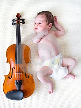 Tiny newborn girl lying next to a violin