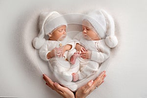 Tiny newborn twin boys in white bodysuits on a white background.