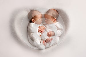 Tiny newborn twin boys in white bodysuits on a white background.