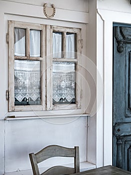 tiny old style vintage house facade with a wooden door and creamy color window with white embroidered curtains, aegean and