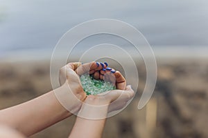 Tiny pieces of plastic collected from sandy beach in hands of environmentalist. Microplastic is polluting the sea and